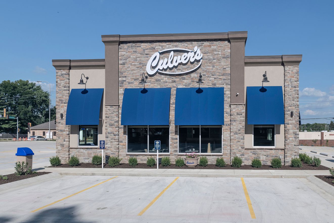 Culver's restaurant building with stone facade, blue awnings, and parking lot on a sunny day.