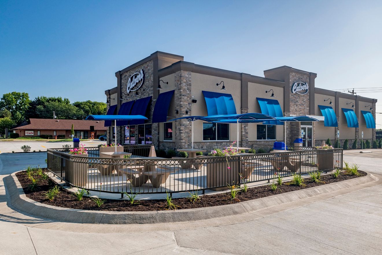 Exterior of a Culver's restaurant with blue awnings, outdoor seating, and a stone facade on a sunny day.