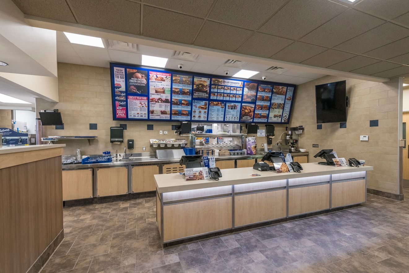 Interior of a fast-food restaurant, with a menu board, counter, and food preparation area.