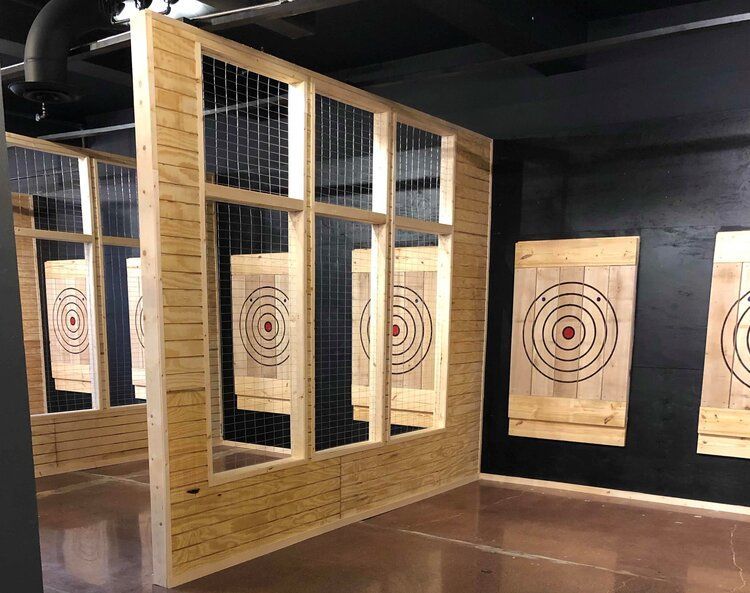 Axe throwing range: Wooden targets in framed lanes with wire mesh backing, indoors with dark walls and floors.