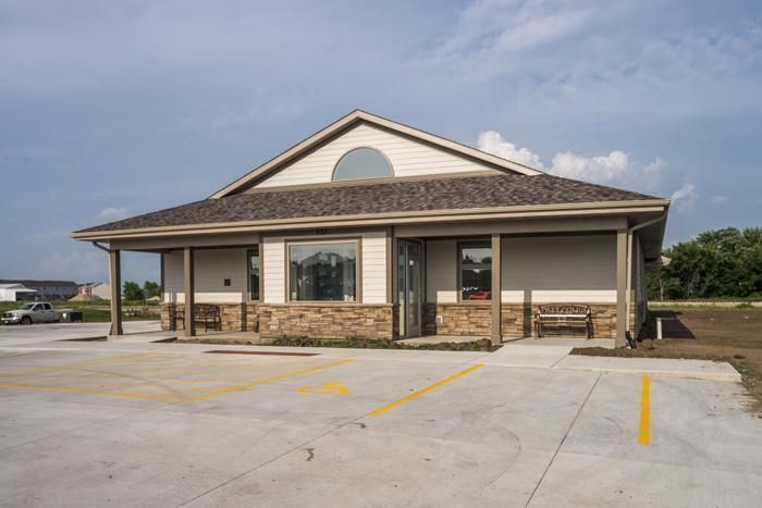 A one-story building with a brown roof and a tan exterior. Paved parking in front.