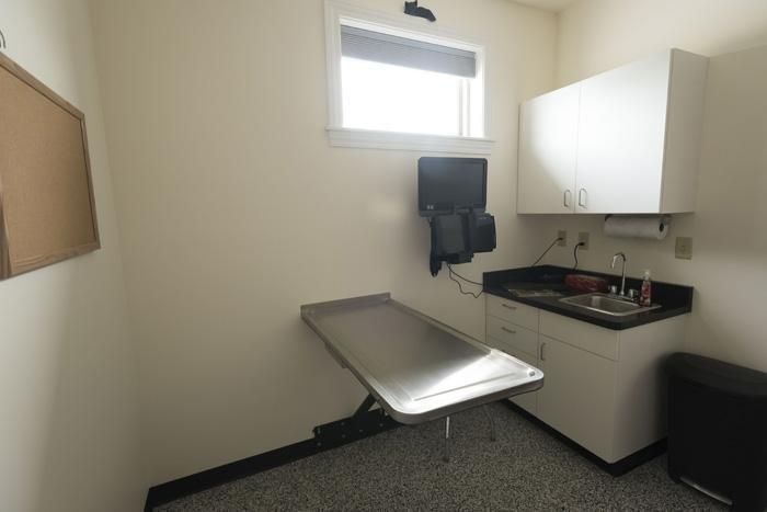 Exam room with stainless steel table, sink, cabinets, window, and bulletin board.