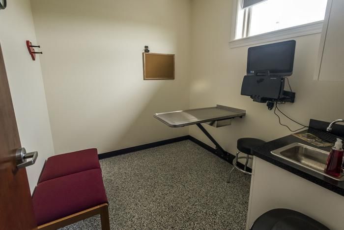 Examination room with stainless steel table, sink, seating, and computer monitor.