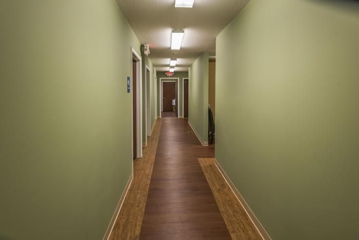 Long hallway with green walls and brown flooring, doors on both sides.