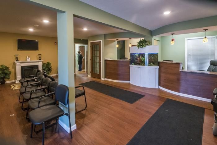 Dental office waiting area with seating, fireplace, reception desk, and person.