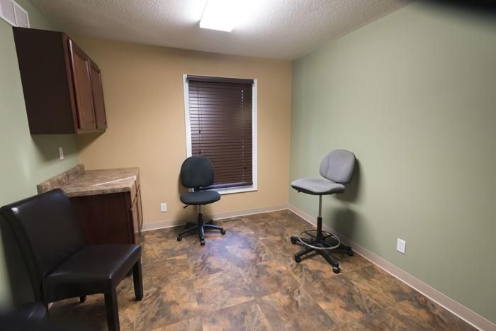 An examination room with two chairs, cabinetry, window with blinds, and brown and green walls.