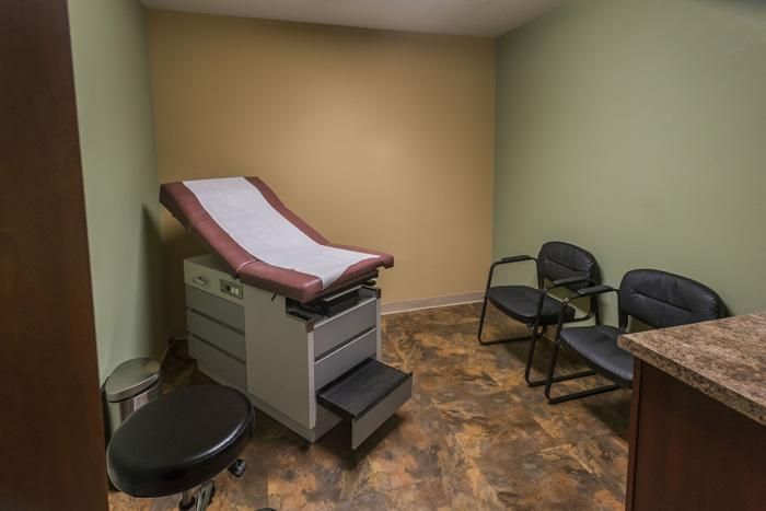 Examination room with examination table, chairs, and medical waste bin.