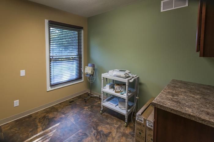 Room with a window, medical cart, and green and tan walls. Brown countertop and a stained concrete floor.