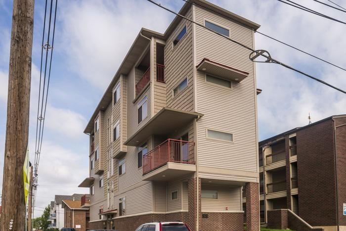 Multi-story tan and brick apartment building with small balconies. Overhead power lines in front.