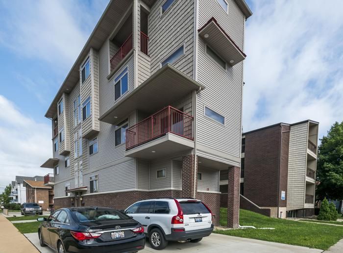 Modern multi-story apartment building with parked cars, brick base, and balconies.