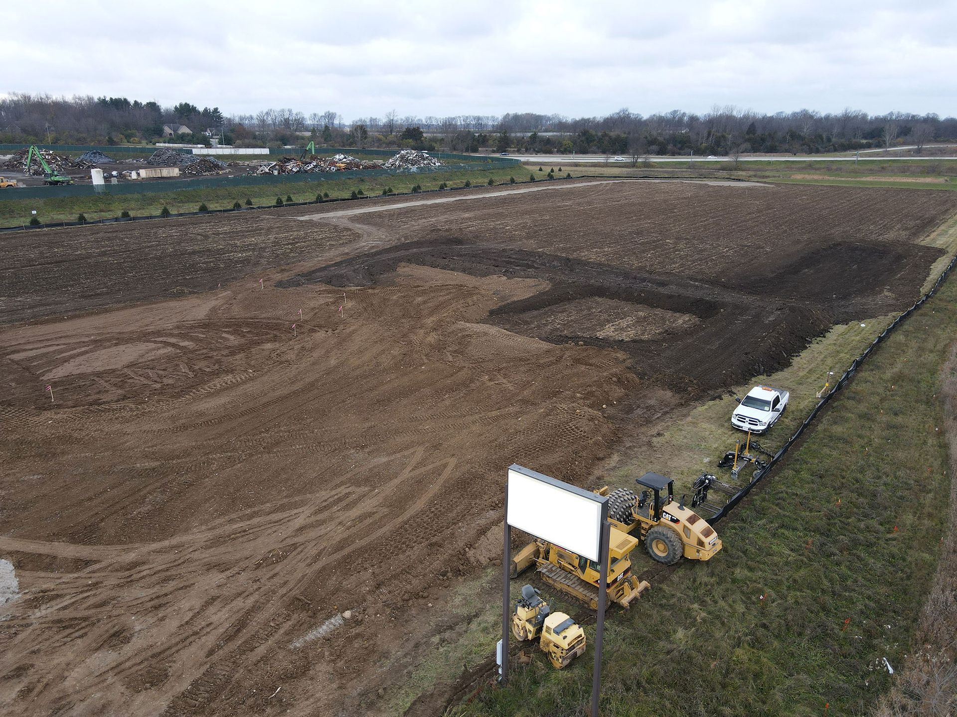 Construction site; earthmovers and a truck on brown field; a blank sign in the foreground.
