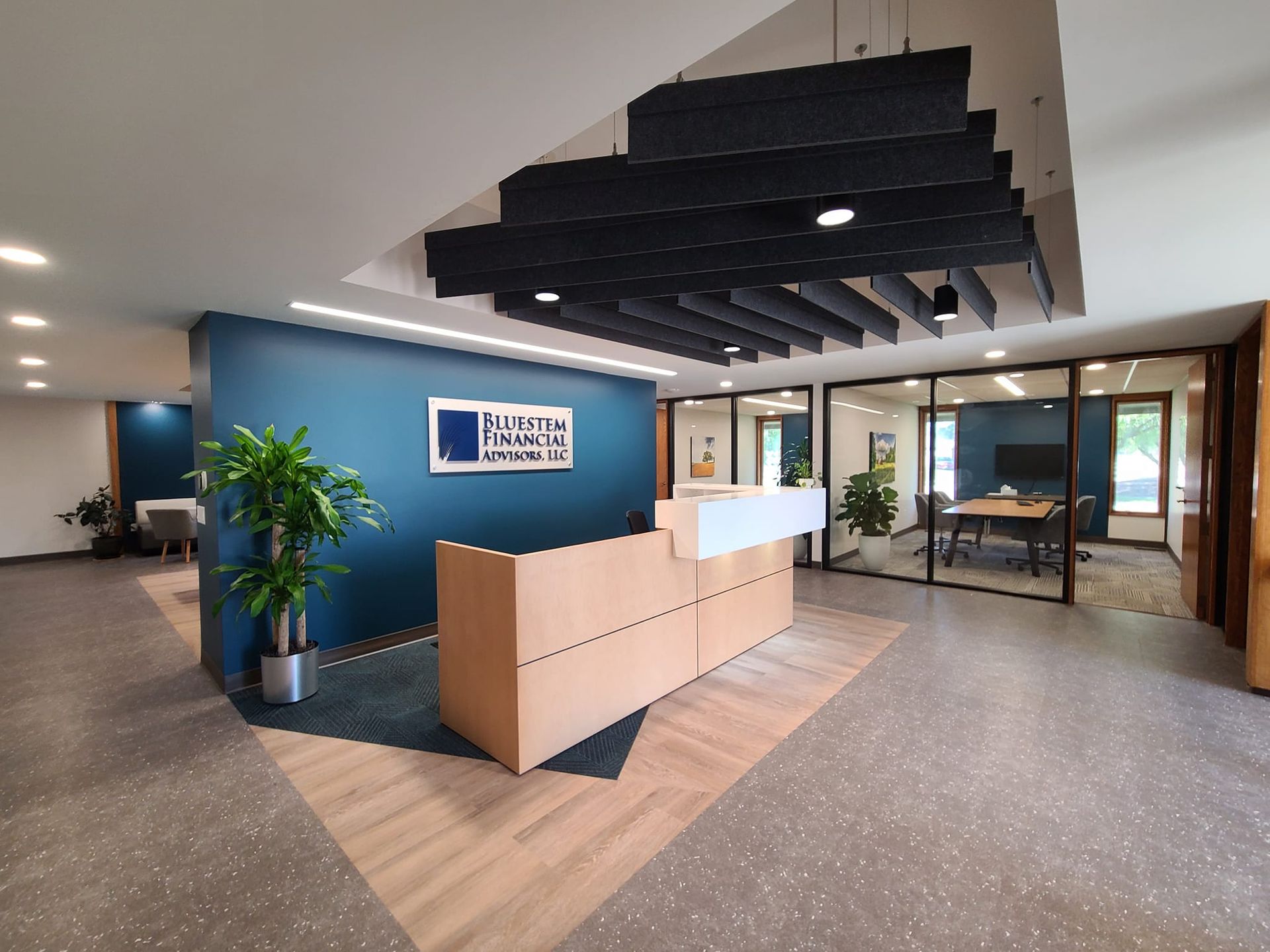 Modern office reception area with blue accent wall, wooden desk, and a conference room.