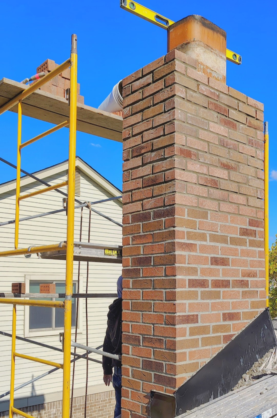 Brown metal roof with brick chimneys against a blue sky.