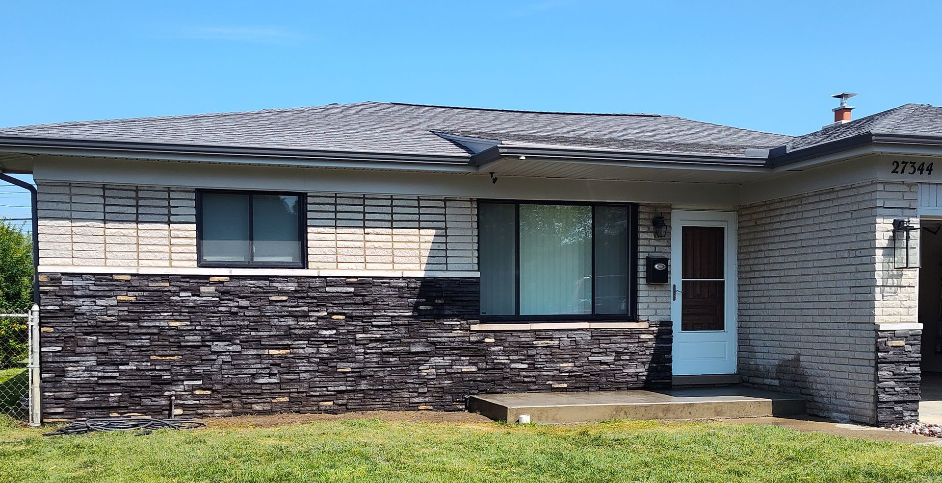 Exterior of a house. Brick facade with black stone on bottom half, windows, and a white front door.