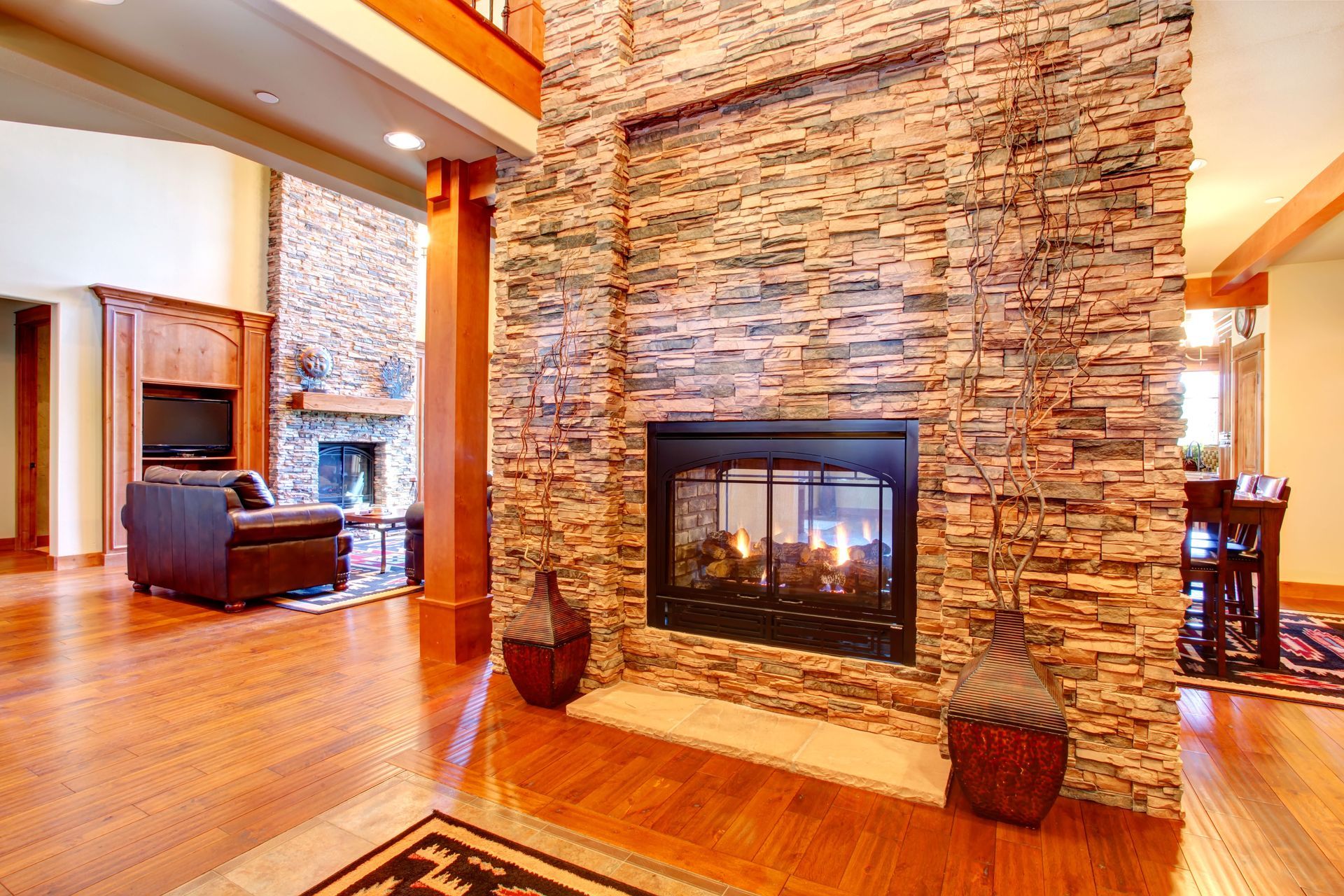 Stone fireplace in a modern home, with a wooden floor and open view to a living room.