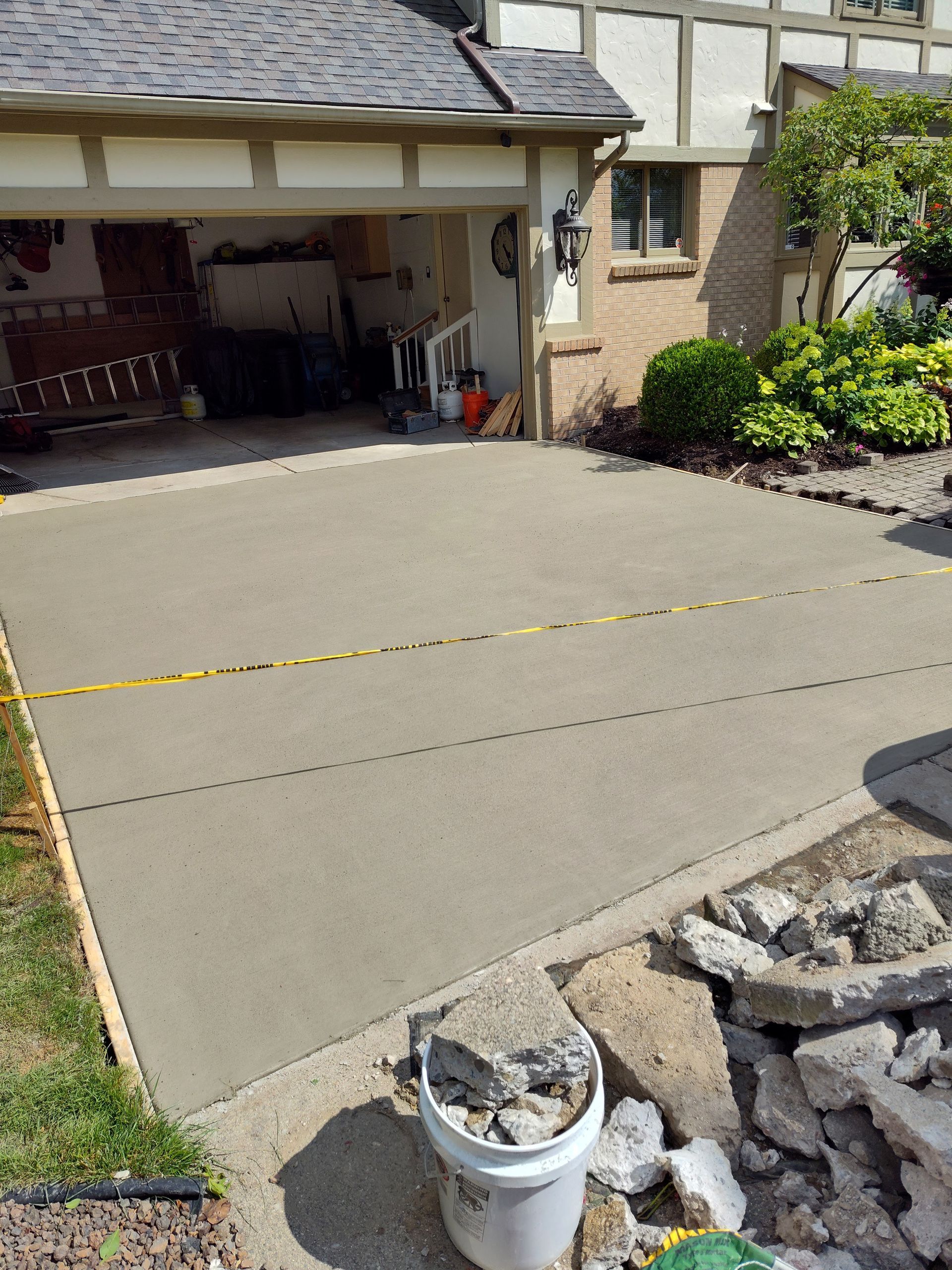 Freshly poured concrete driveway in front of a house and garage; yellow tape present.