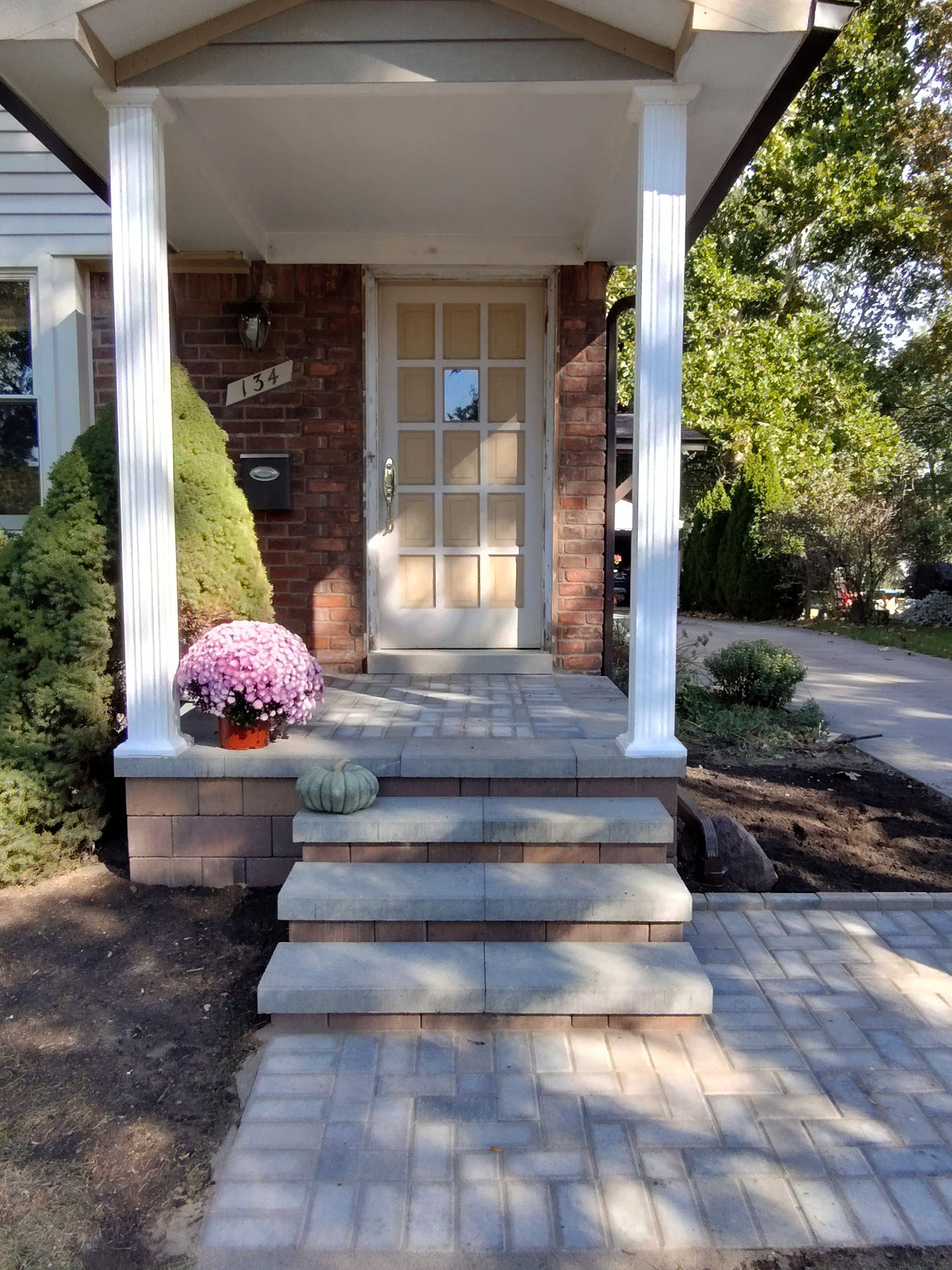 Front porch with stone steps, brick facade, white columns, and pink flowers.