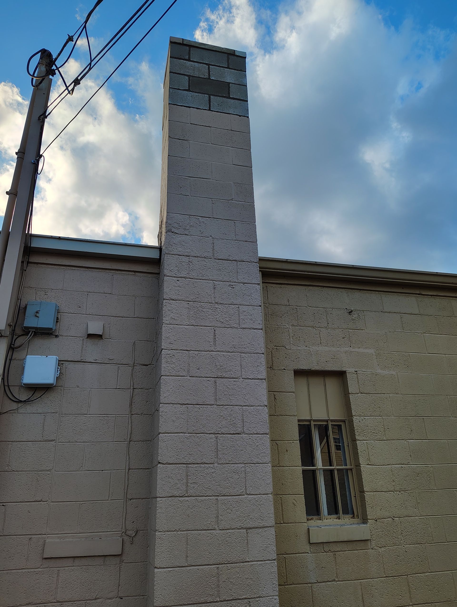 Tall brick chimney extending from a light-colored building under a cloudy sky.