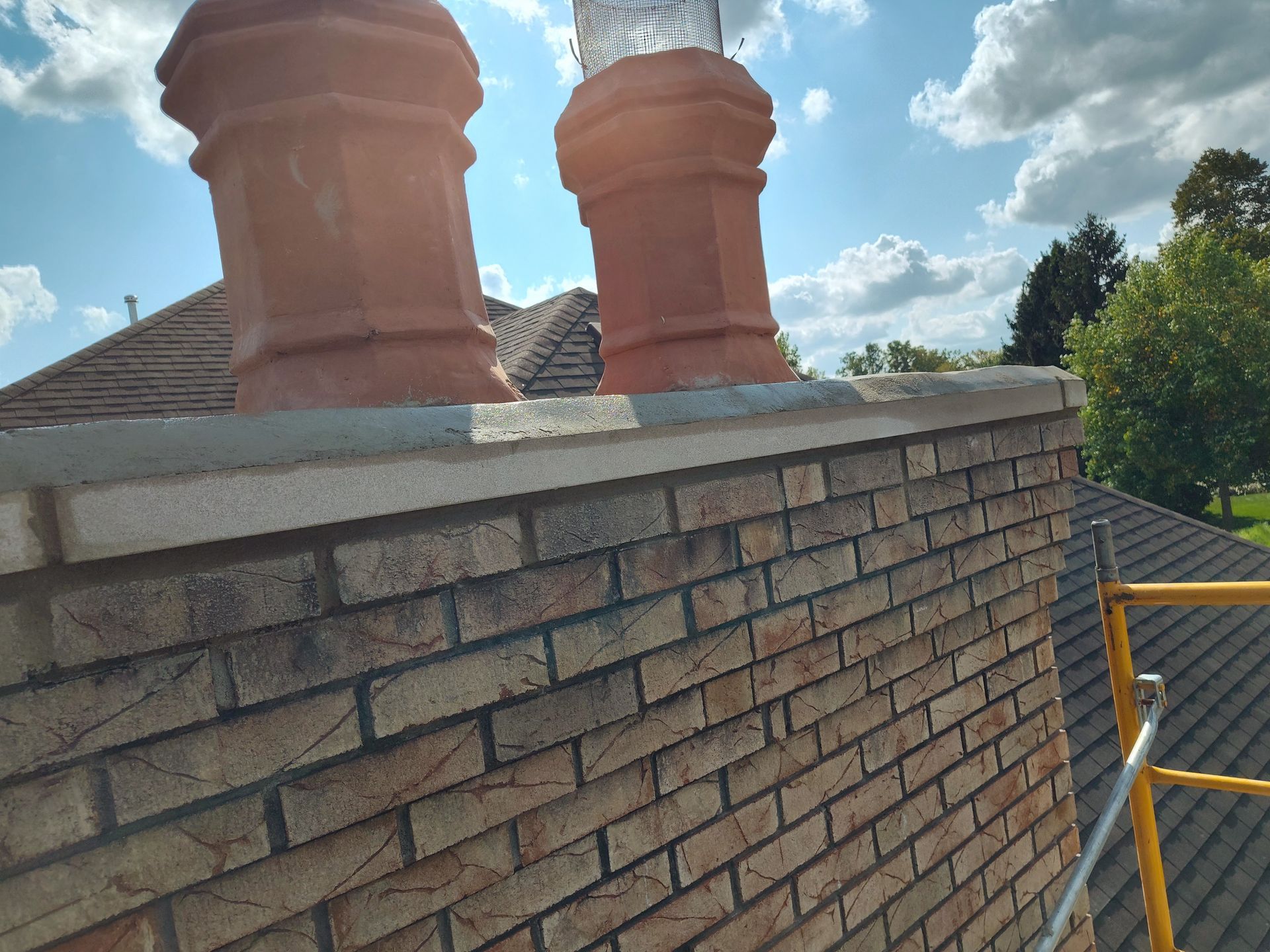 Brick chimney with two terracotta chimney pots on a rooftop under a bright sky.