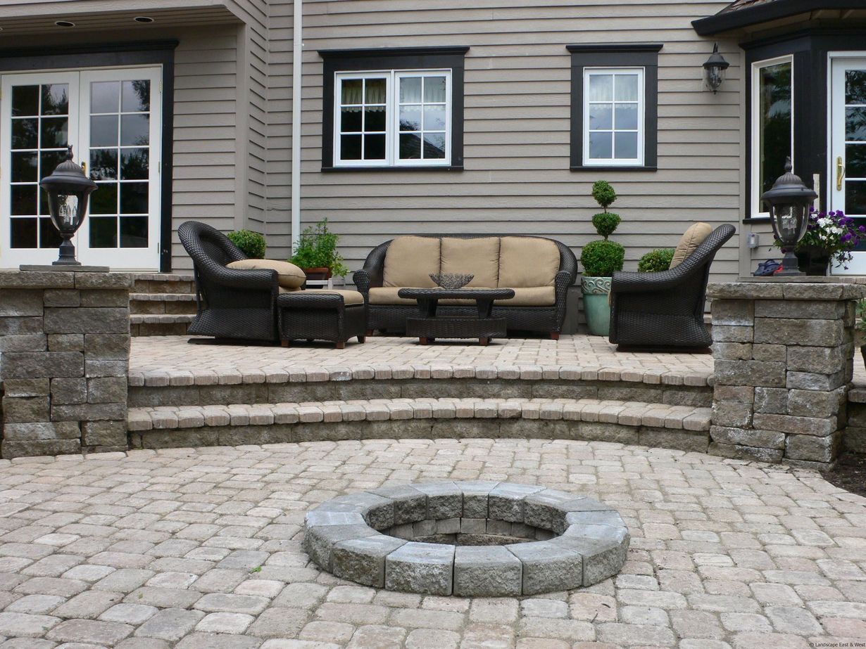 Patio with outdoor furniture, stone fire pit, and a house in the background.