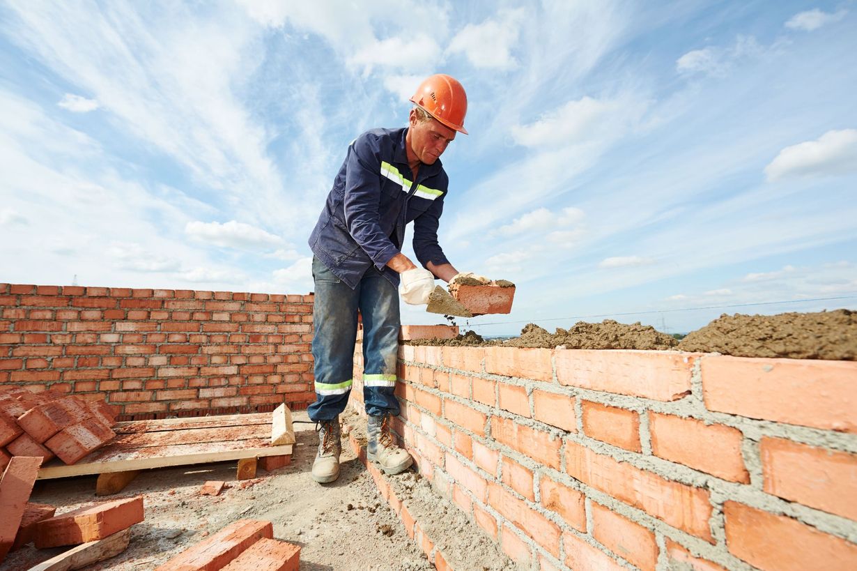 Construction worker laying bricks on a wall, wearing safety gear, outdoors.