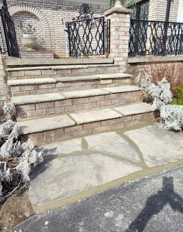 Stone steps with light-colored treads and brick risers leading up to a brick porch with decorative metal railings.