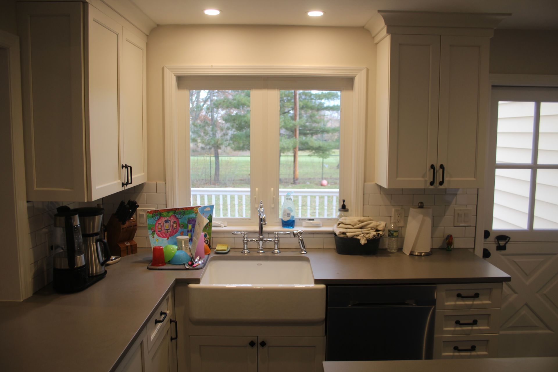 A kitchen with white cabinets, a sink, a dishwasher, and a window.