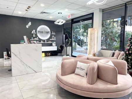 Salon interior with pink seating, marble front desk, and black wall.