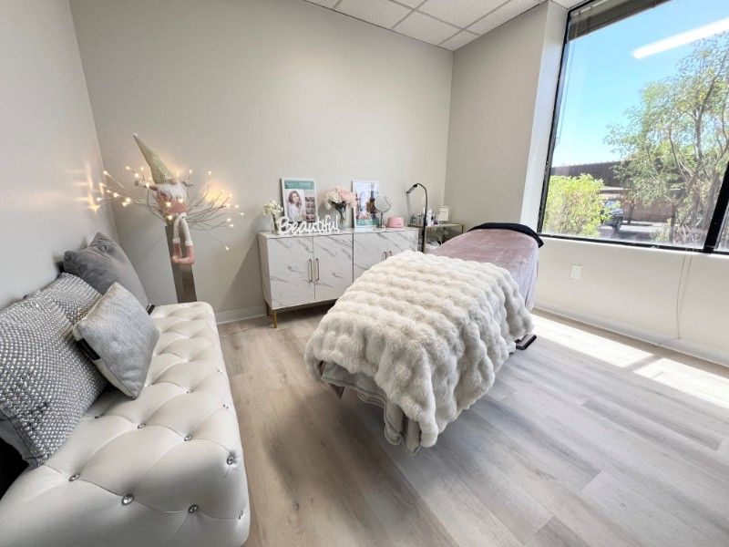 Spa treatment room with a white tufted bench, marble cabinet, and a bed covered in a fluffy blanket.