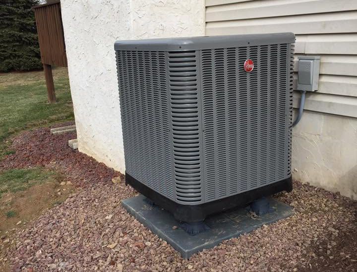 Gray outdoor air conditioner unit beside a house on a gravel bed