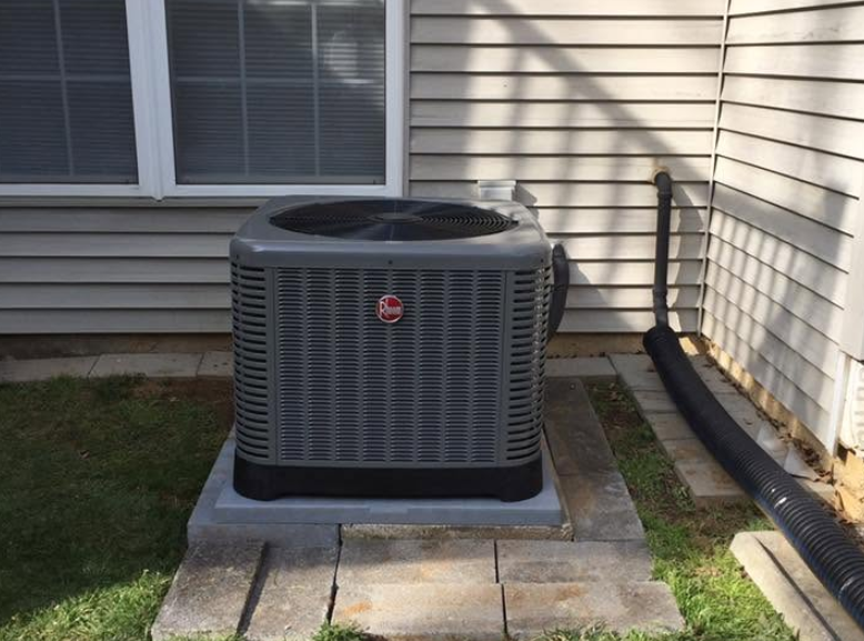 Outdoor air conditioner unit beside a house on a concrete pad near siding and grass