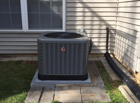 Outdoor air conditioner unit beside a house on a concrete pad near siding and grass