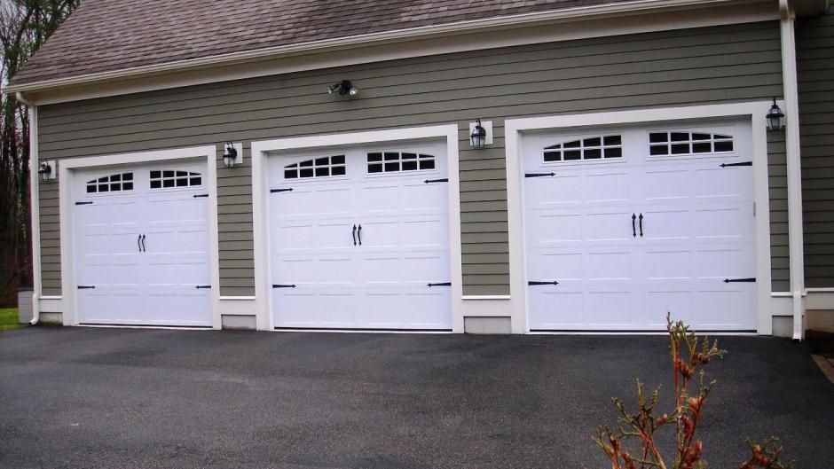 Three white garage doors are lined up in front of a house.