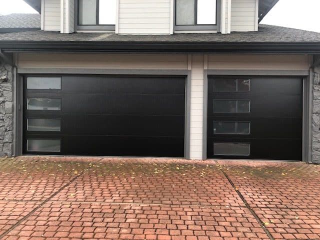 A house with a black garage door and a brick driveway.