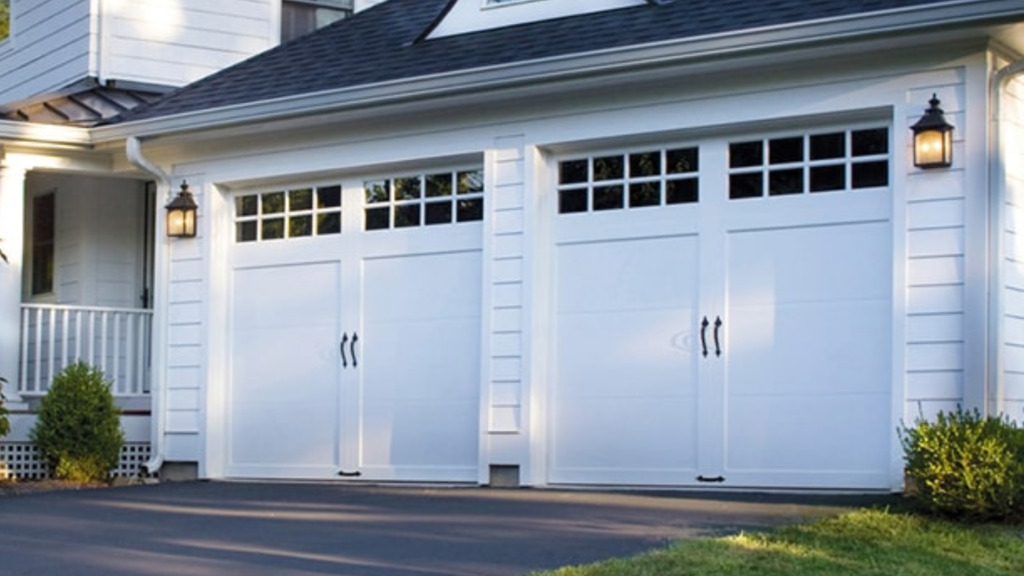 A white house with three white garage doors and a black roof.