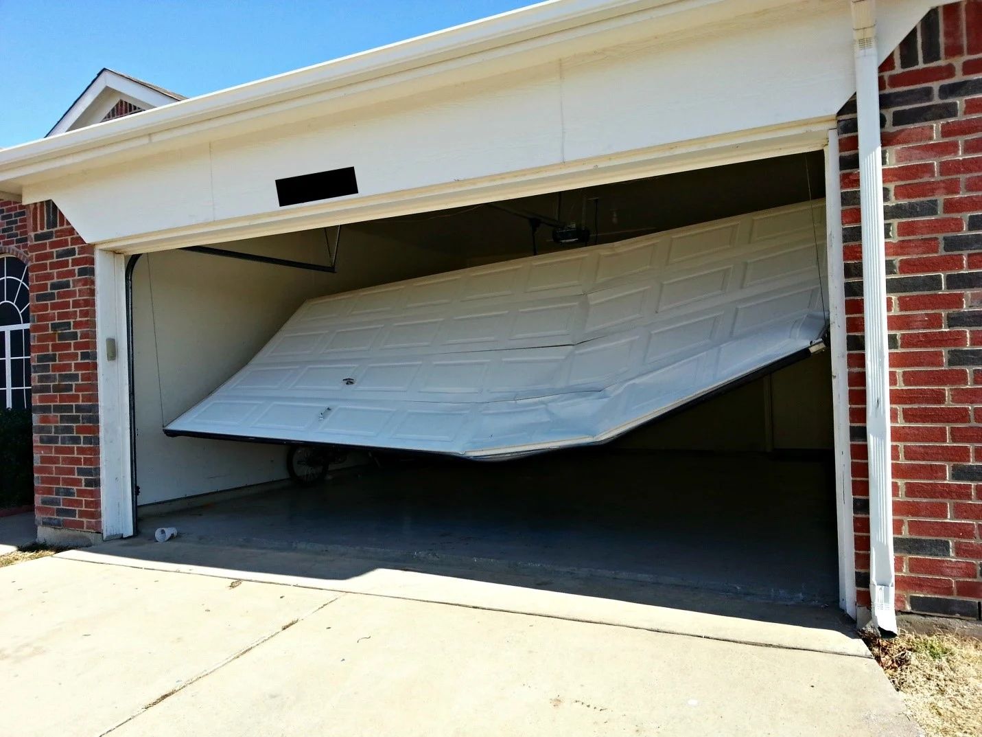 A broken garage door is open in front of a brick house.