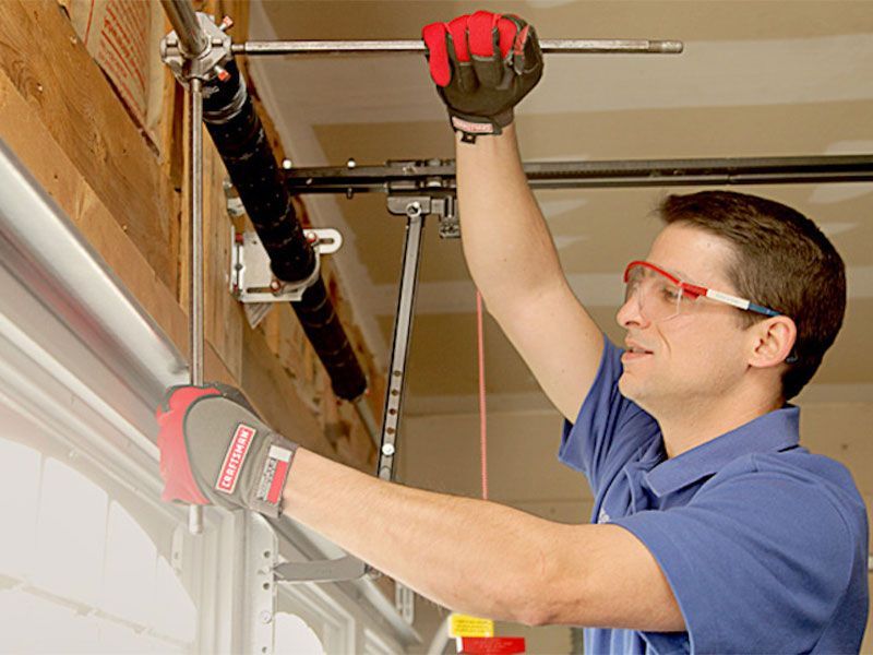 A man wearing gloves and goggles is working on a garage door.