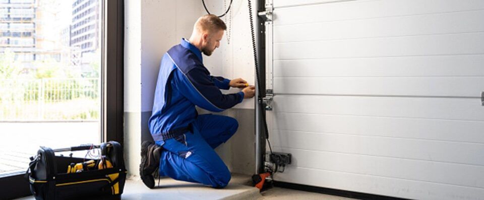 A man is kneeling down in a garage fixing a garage door.