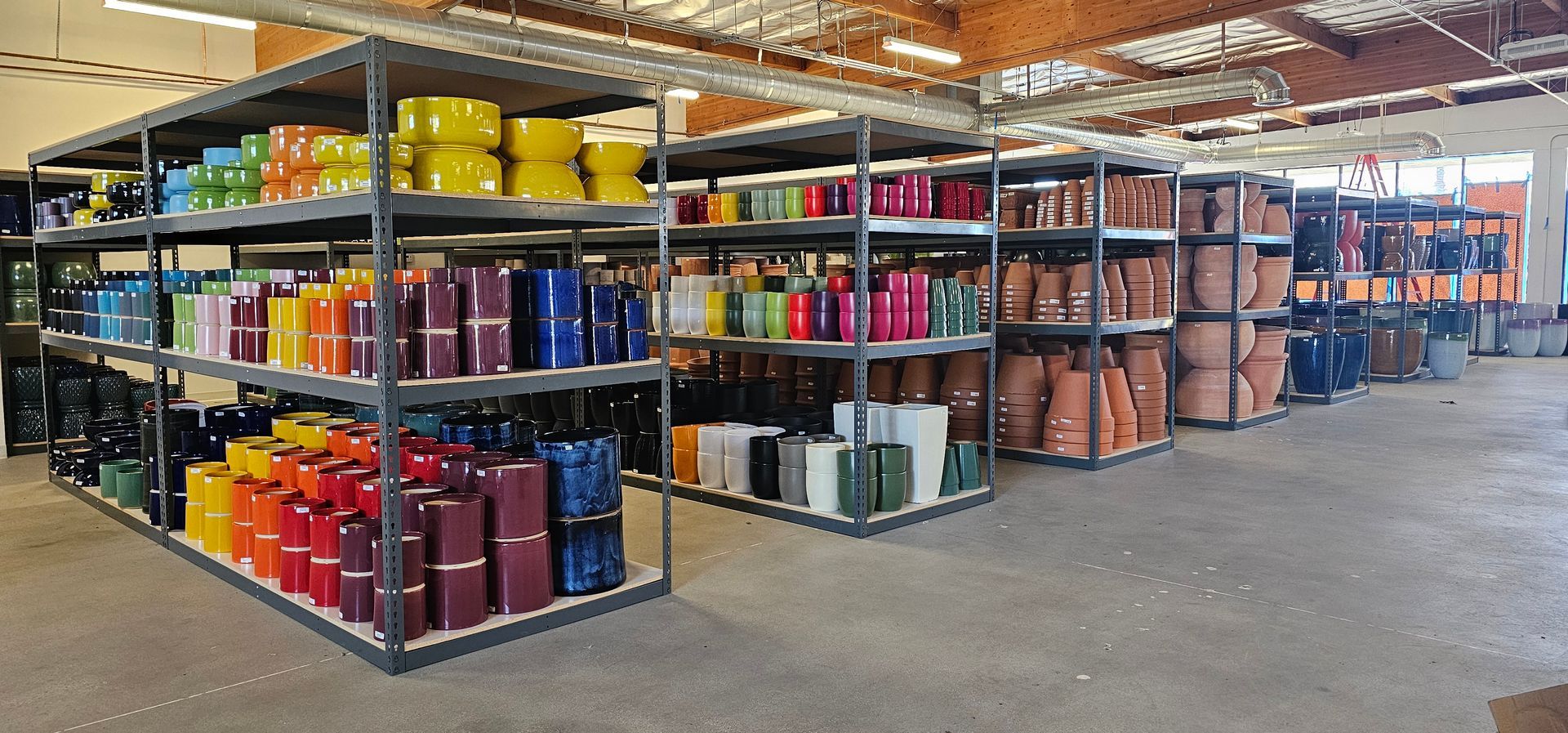 A warehouse with metal shelves displaying colorful ceramic pots and planters.
