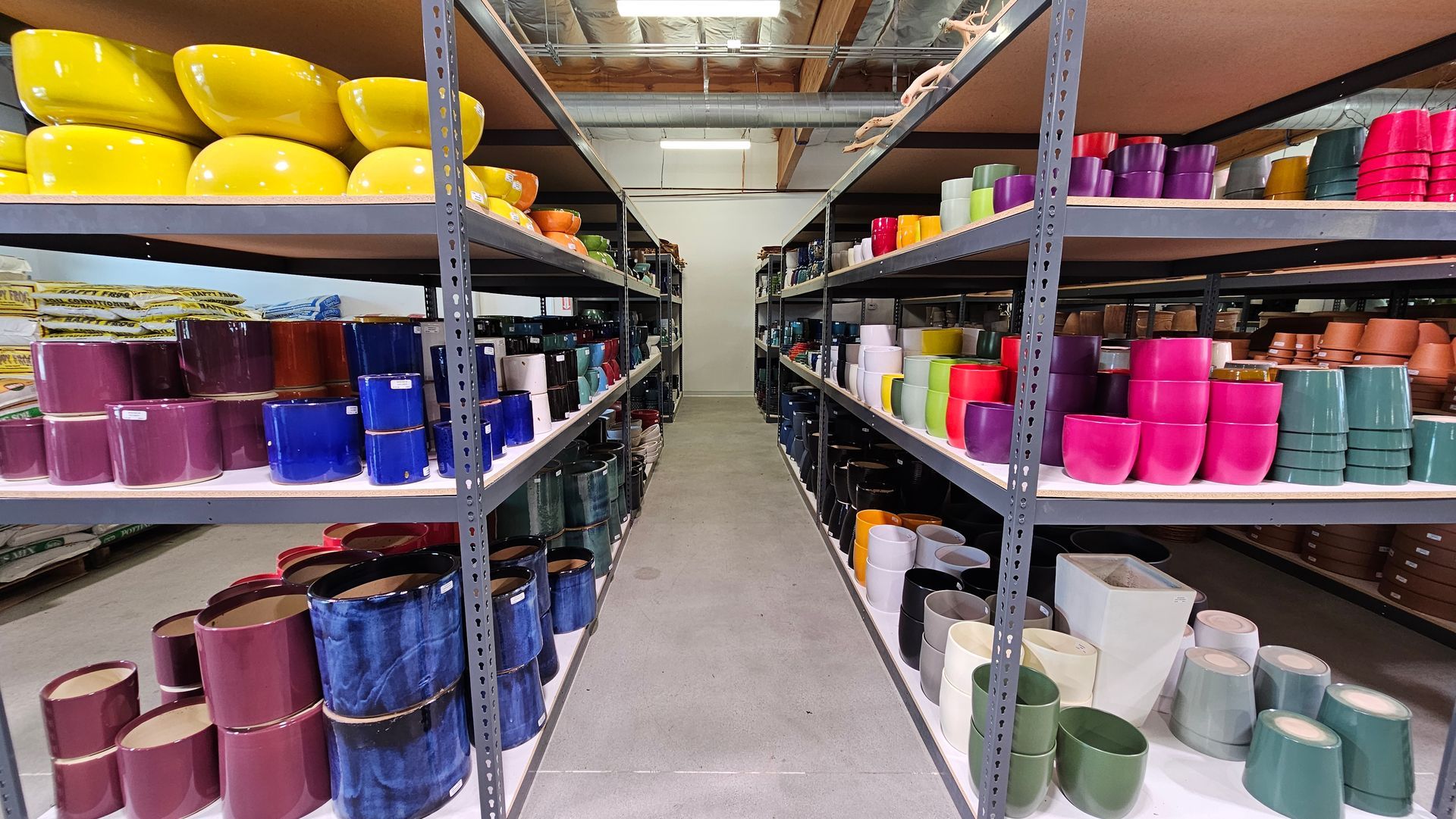 Rows of colorful ceramic pots on metal shelves in a warehouse.