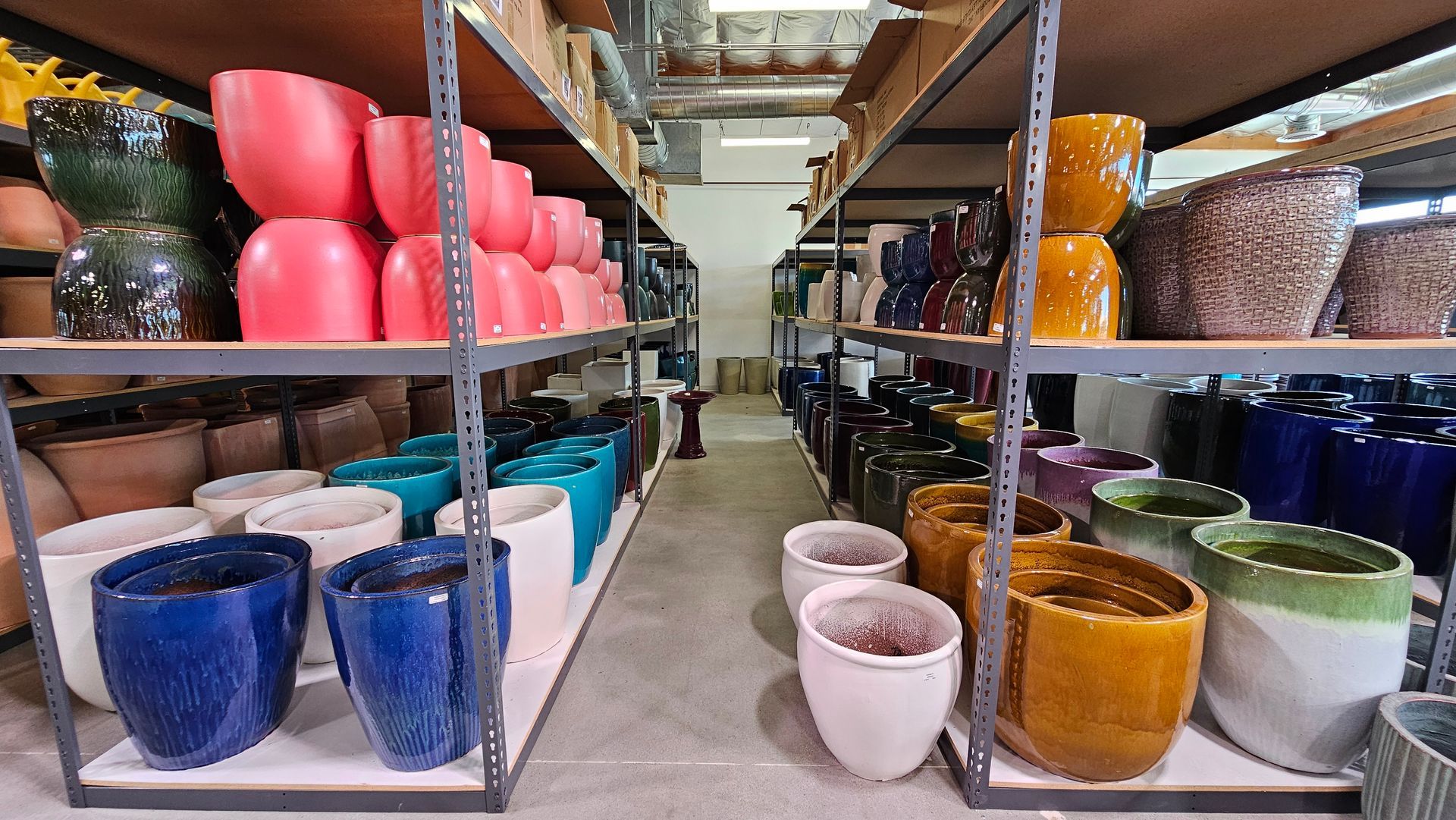 Shelves filled with colorful ceramic pots of various shapes and sizes inside a warehouse.
