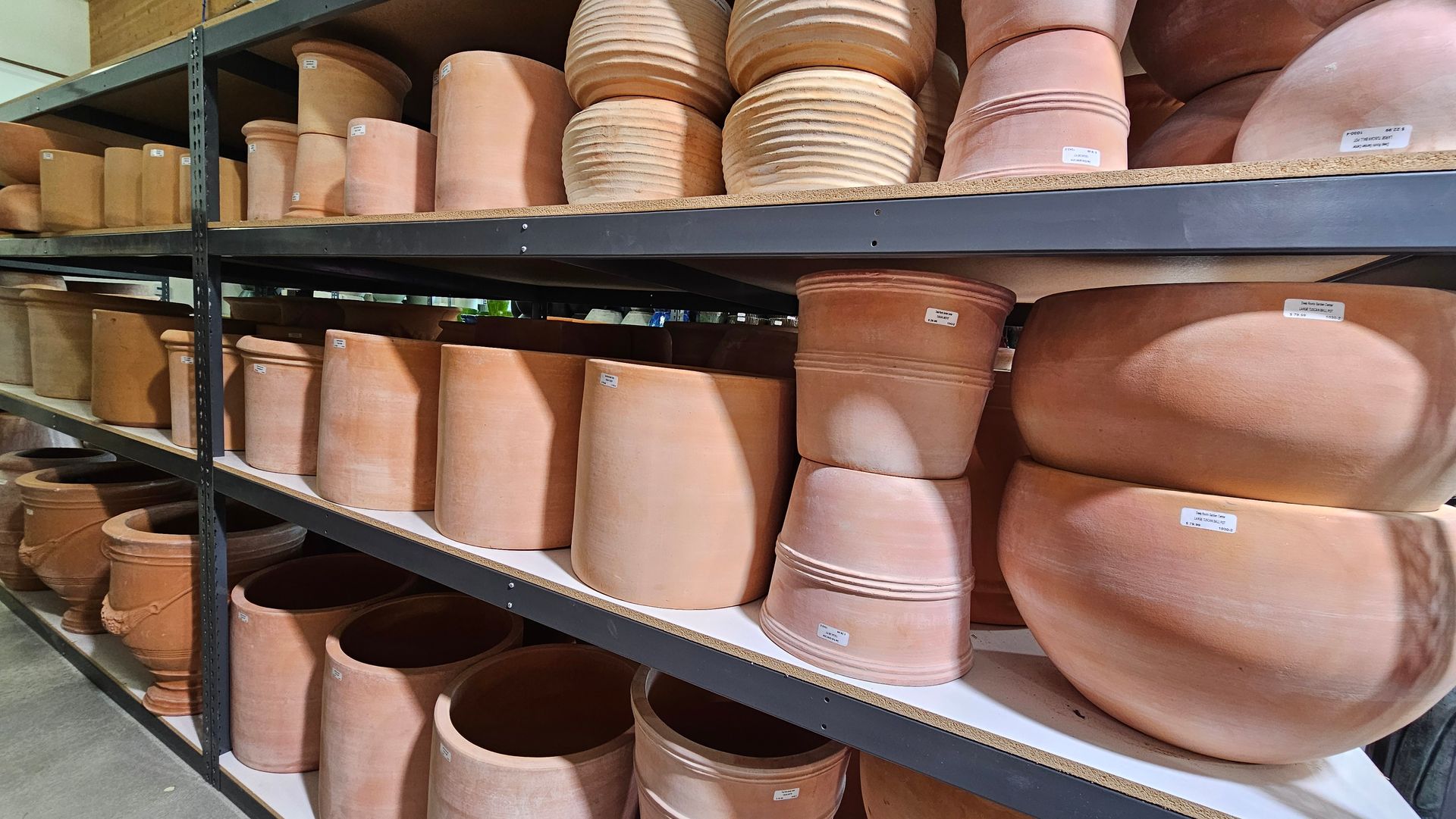 Shelves filled with various terracotta flower pots in shades of brown, inside a shop or warehouse.