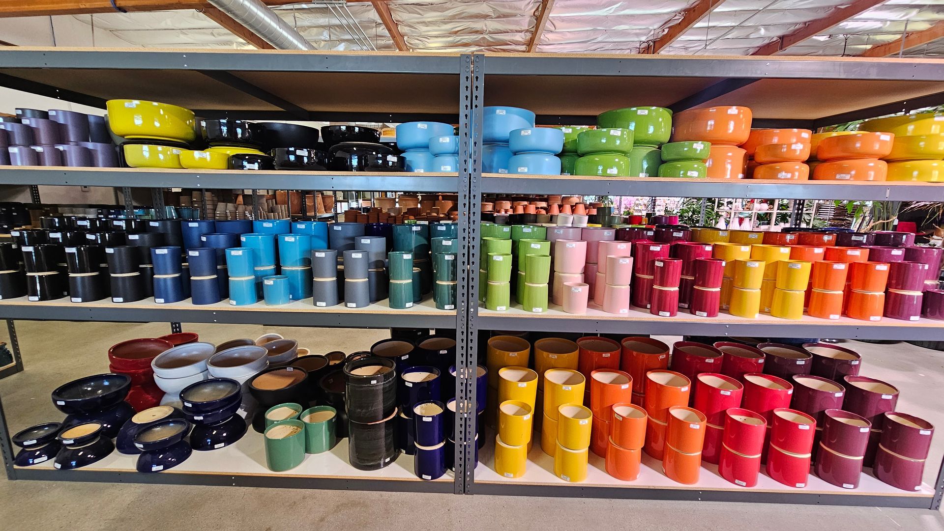 Shelves of colorful ceramic planters in various shapes and sizes, arranged by color in a warehouse.