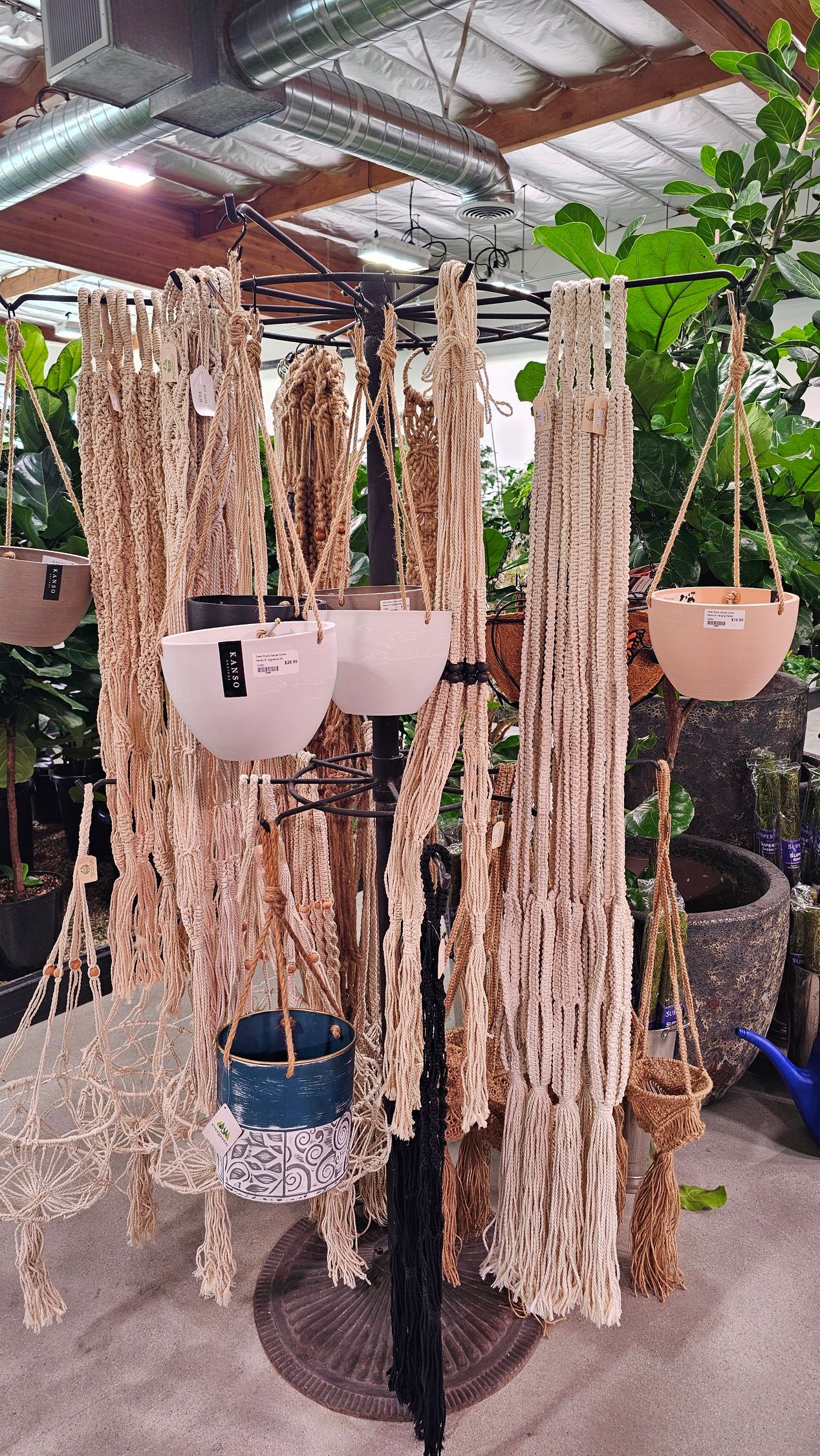 A display of hanging planters in a shop. Tan and white pots hang from a black stand and ropes, with dried foliage.