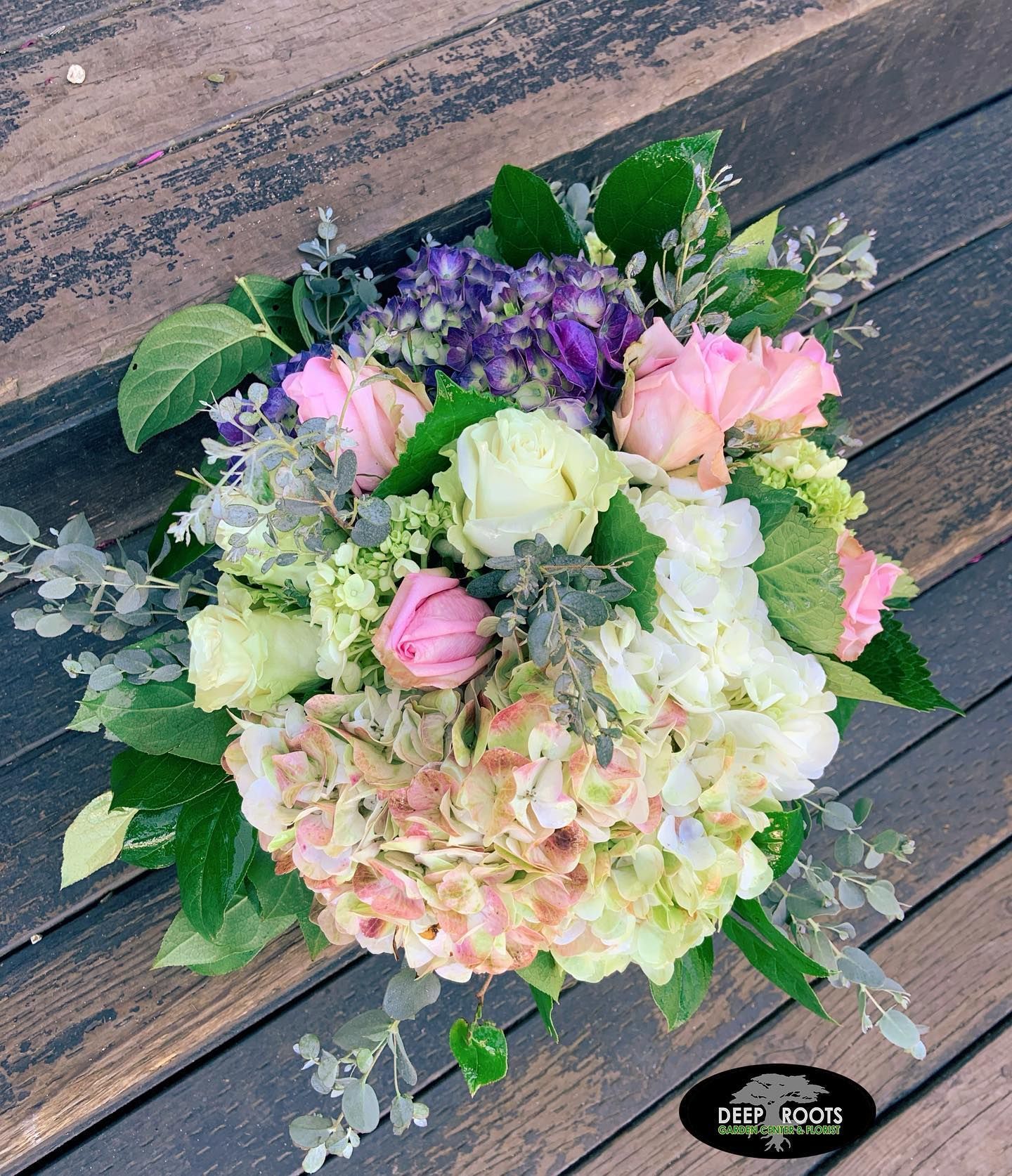 Bouquet of pink, white, and purple flowers, including hydrangeas, on a wooden surface.