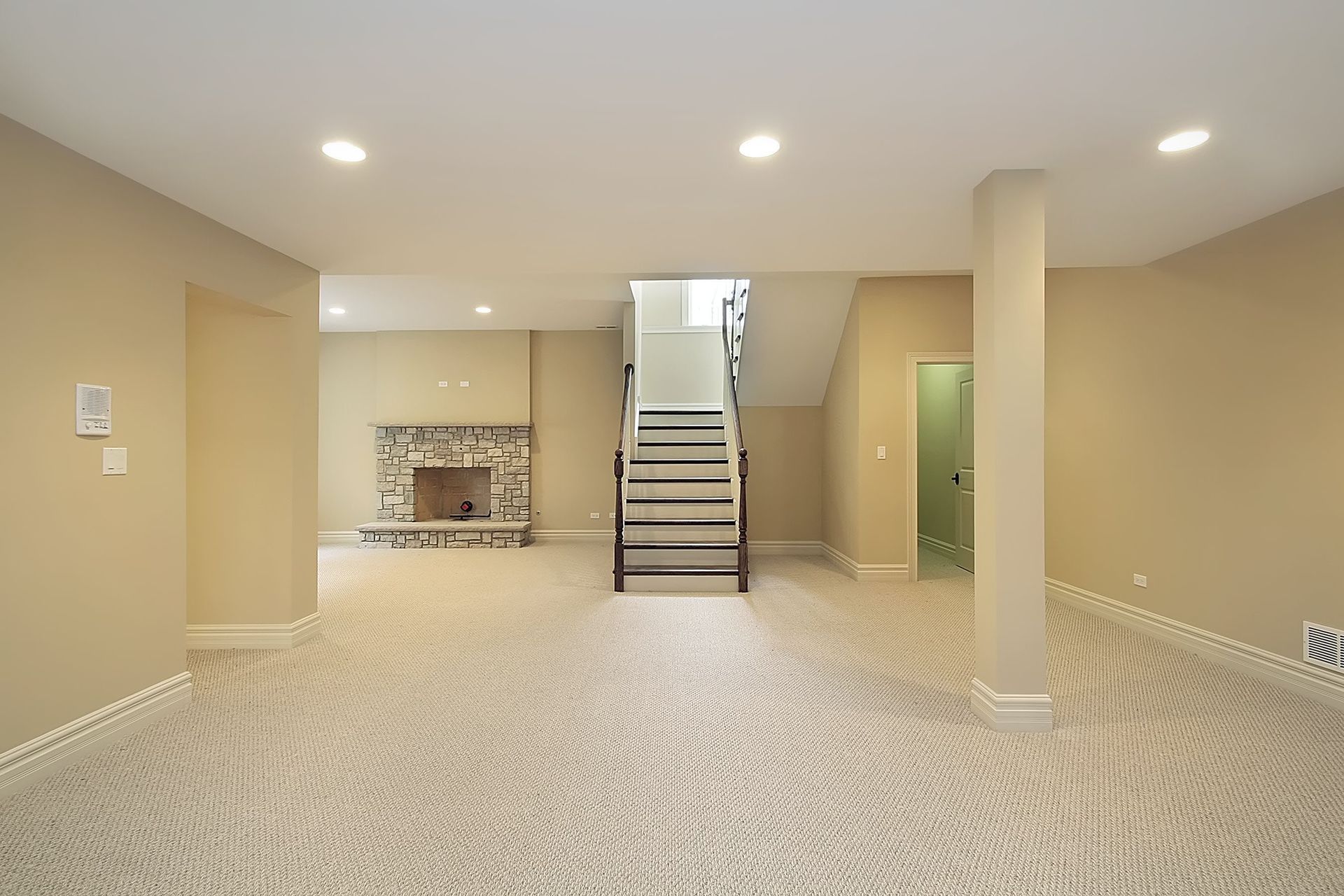 Empty basement with carpet, stairs, fireplace, and support column. Beige walls and recessed lighting.