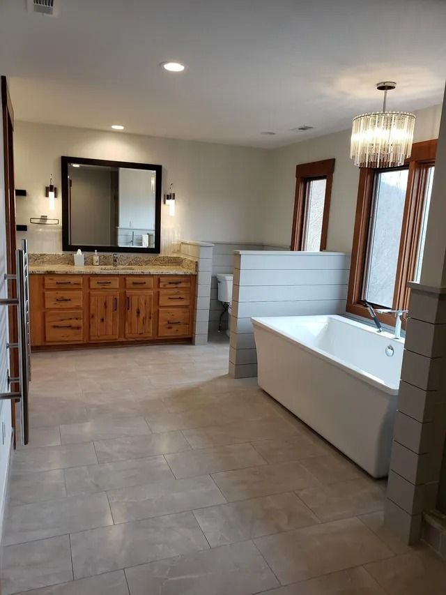 Spacious bathroom with white tub, wood vanity, and tile floor.