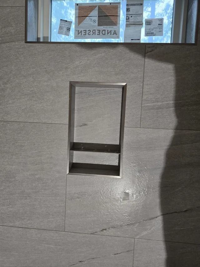 Recessed shelf built into a tiled shower wall. Stainless steel trim.