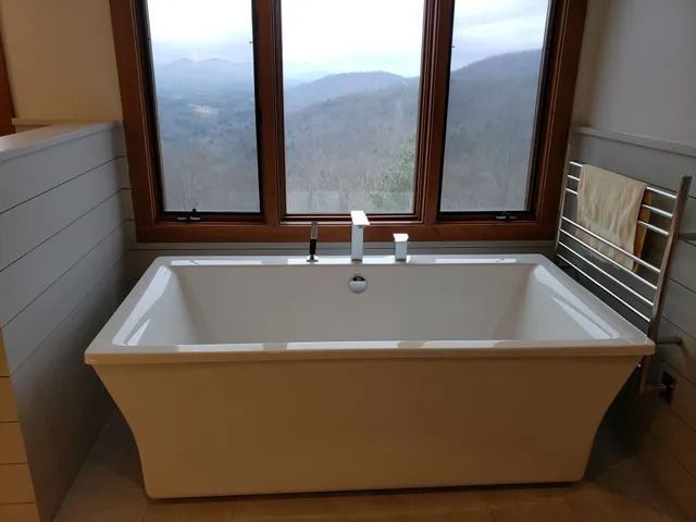 White bathtub in front of a window with a mountain view, chrome faucet, and towel rack.