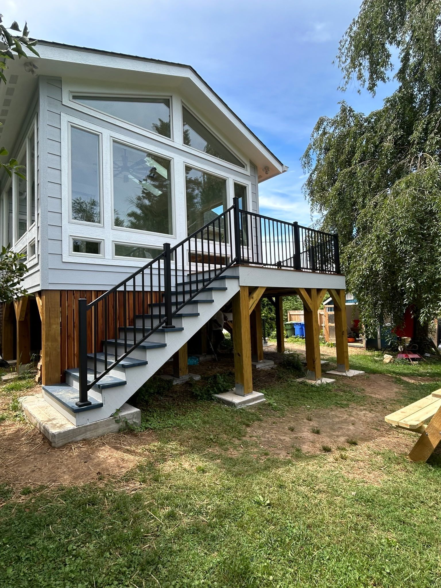 Raised white house with black stairs and porch, built on stilts in a wooded yard